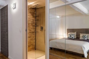 A modern bedroom with a glass partition, a shower area with a stone wall, and a bed with white bedding. - Beautiful loft between Old Nice and the port (Niza)
