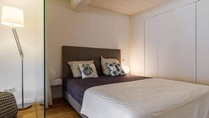Un dormitorio con cama, mesita de noche, lámpara y armario.