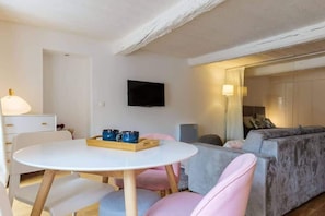 A modern living room with a white round table, pink and grey chairs, a grey sofa, and a flat-screen TV mounted on the wall. - Beautiful loft between Old Nice and the port (Niza)
