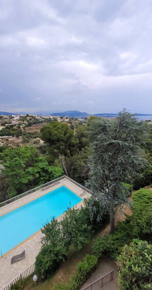 A swimming pool surrounded by greenery, with a view of a town and mountains in the distance.