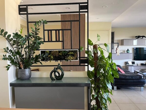 A modern living room with a sofa, a coffee table, and a TV. There is a decorative wall panel and a potted plant on the left.