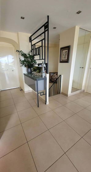 A spacious room with a tiled floor, a staircase, a potted plant, and a framed picture on the wall.