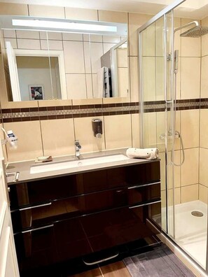 A bathroom with a glass shower enclosure, a sink with a mirror above, and a towel on the counter.