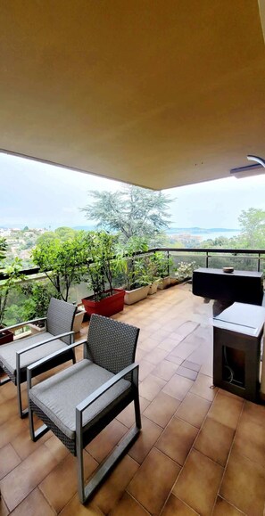A balcony with tiled flooring, outdoor furniture, potted plants, and a television.