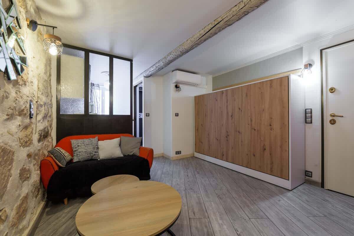 A modern room with a stone wall, a wooden floor, a sofa with cushions, a round table, and a large wooden wardrobe.