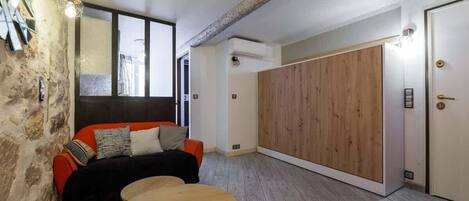 A modern room with a stone wall, a wooden floor, a sofa with cushions, a round table, and a large wooden wardrobe.