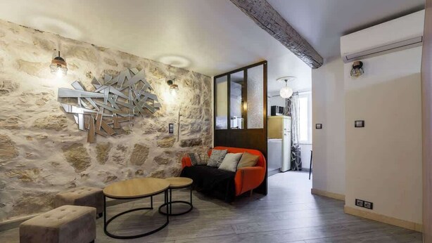 A room with a stone wall, a red sofa, a wooden coffee table, and a small ottoman. - Cosy studio place du pin (Niza)
