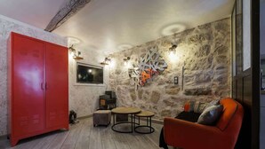 A room with a stone wall, a red wardrobe, a round table, a sofa, and a TV. - Cosy studio place du pin (Niza)