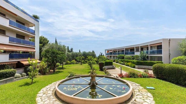 A courtyard with a central fountain, surrounded by well-maintained lawns and a modern building with balconies. - Comfortable Apartment with large sunny terrace (Niza)