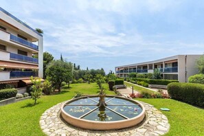 A courtyard with a central fountain, surrounded by well-maintained lawns and a modern building with balconies.