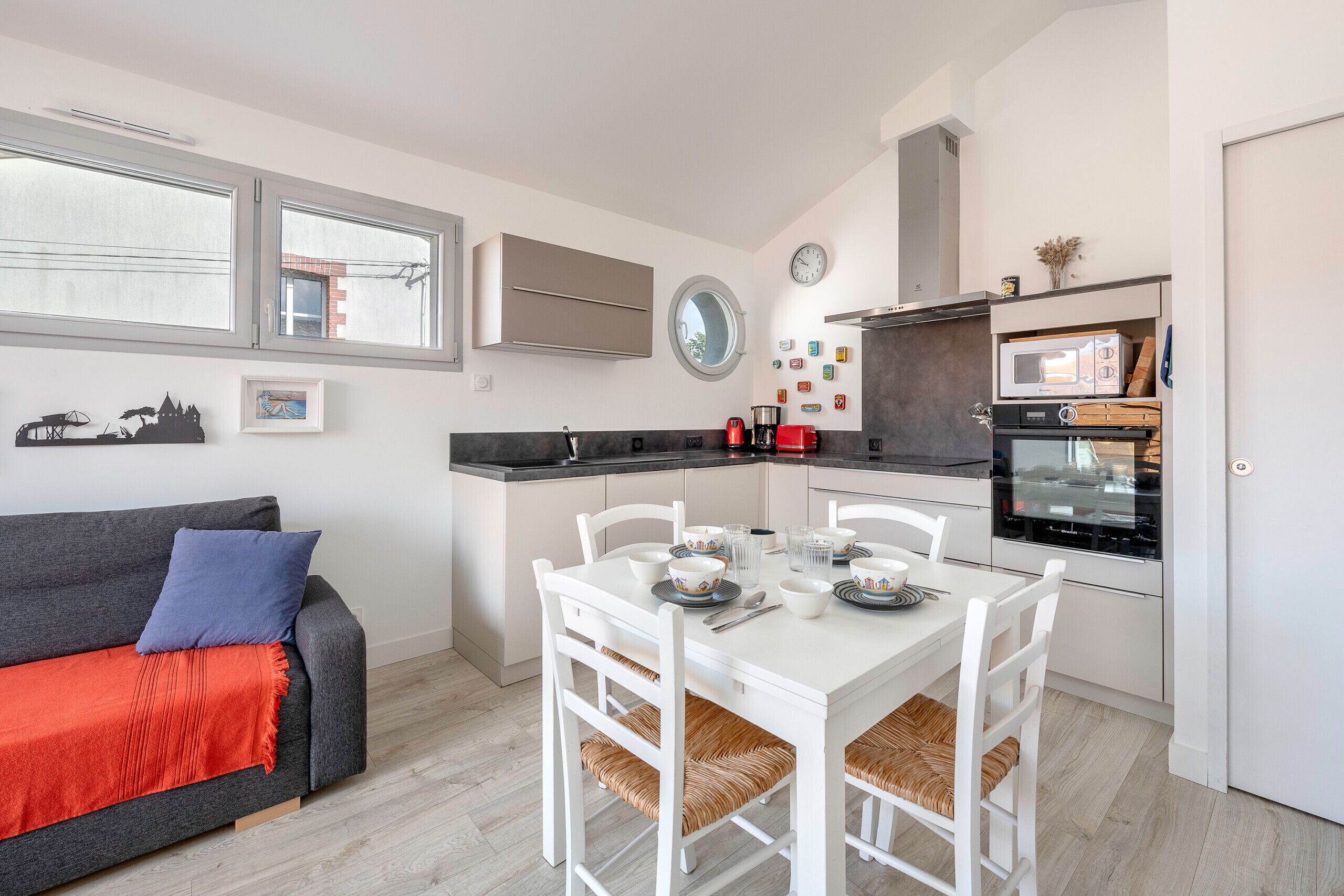 A compact living space with a kitchenette, a dining area, and a sofa with a red throw blanket.
