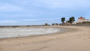 Una playa con arena, un edificio pequeño y algunos árboles.