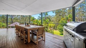 Une terrasse extérieure avec une table et des chaises en bois, un barbecue et une vue sur un paysage verdoyant.