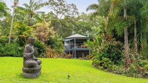 Un jardin paisible, orné d’une statue de Bouddha, d’une végétation luxuriante et d’un bâtiment à deux étages.