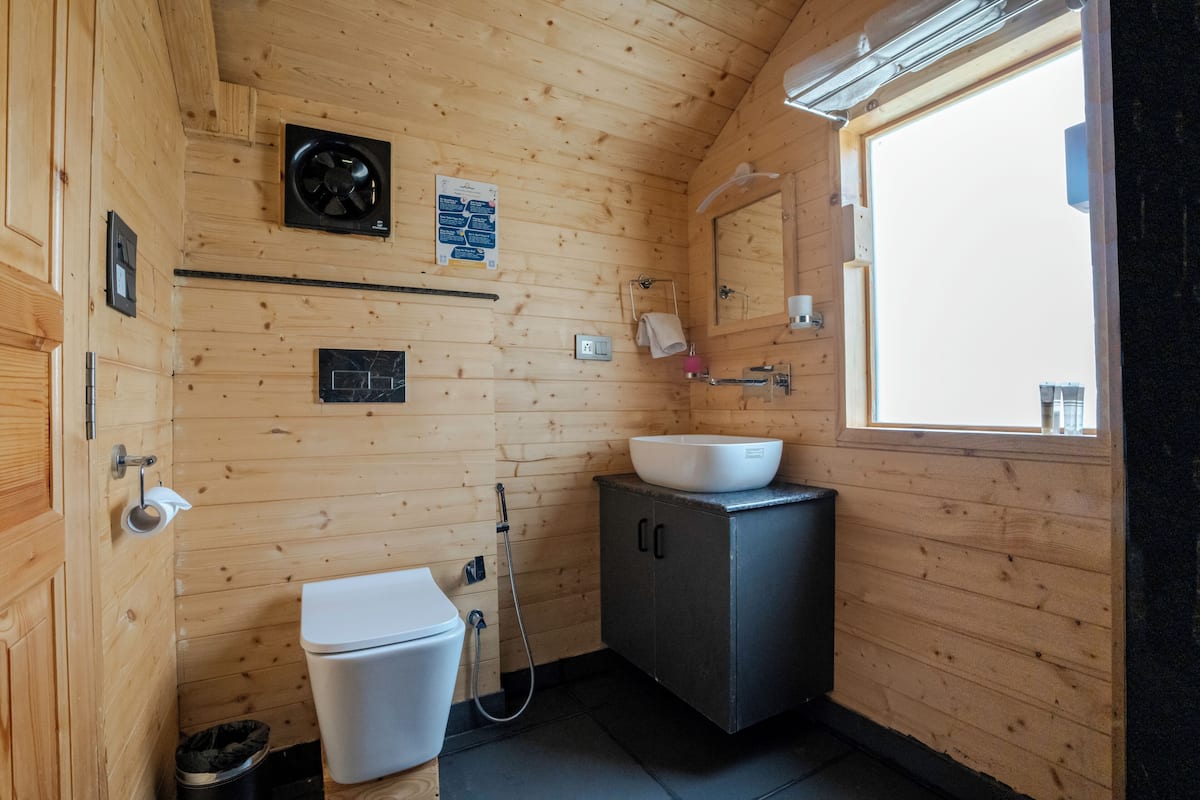 Baño de una cabaña de madera con inodoro, lavabo y ducha.