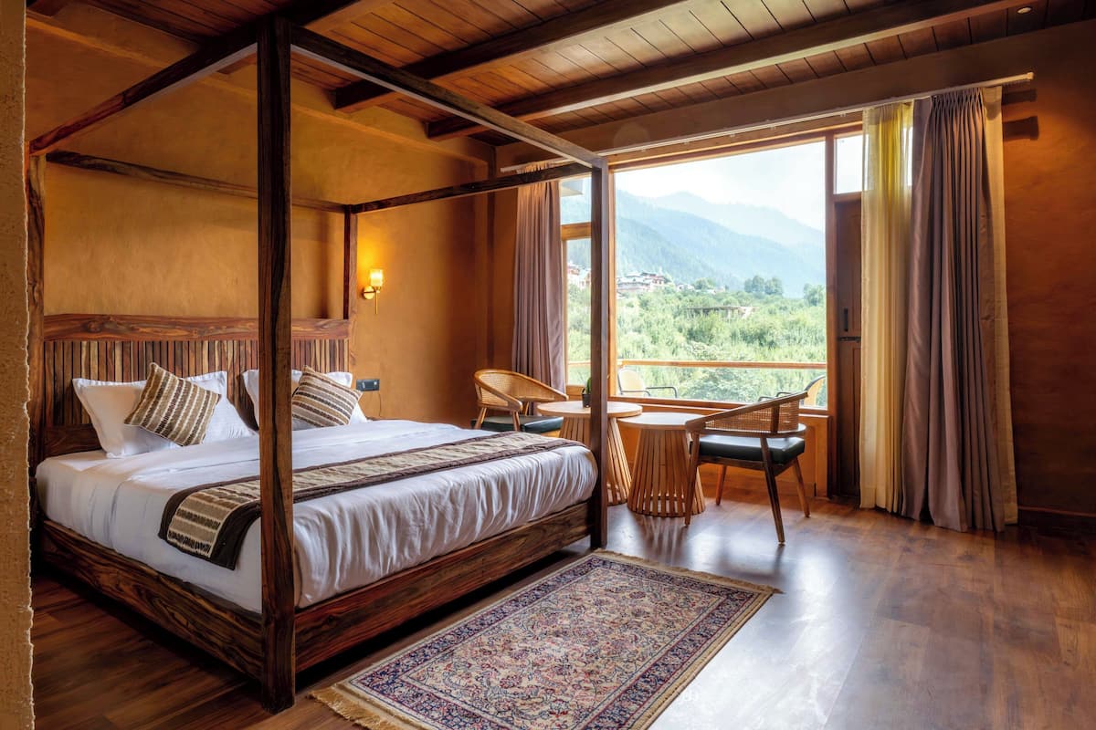 Una cama con dosel con vistas a montañas, una pequeña mesa redonda con sillas y suelo de madera.