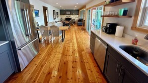 Een moderne keuken met houten vloeren, roestvrijstalen apparatuur en een eethoek met een tafel en stoelen.