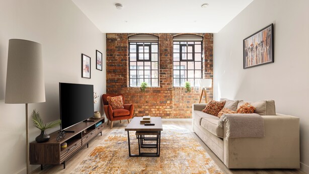 A living room with a brick wall, a flat-screen TV, a sofa, a coffee table, and a floor lamp. - The Brickworks - Grade II Boutique Stay, 2 Bed. (Birmingham)