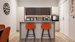 A modern kitchen with a central island, two bar stools, and a dining table with chairs. - The Brickworks - Grade II Boutique Stay, 2 Bed. (Birmingham)