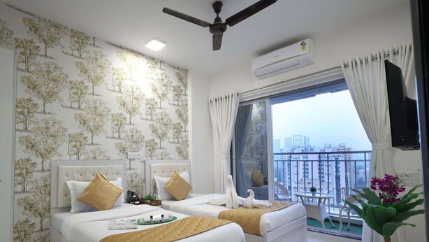 A modern bedroom with two beds, a ceiling fan, an air conditioning unit, and a balcony with a city view. - 2 BHK HomeSuite (Gagal Home) (Mumbai)