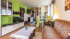 Una sala de estar moderna con una pared verde, un televisor de pantalla plana, un sofá estampado de leopardo y un comedor con mesa de vidrio.