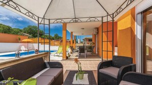 Un espacio exterior cubierto con mobiliario de mimbre, una planta en maceta y vistas a una piscina y zona de comedor al aire libre.