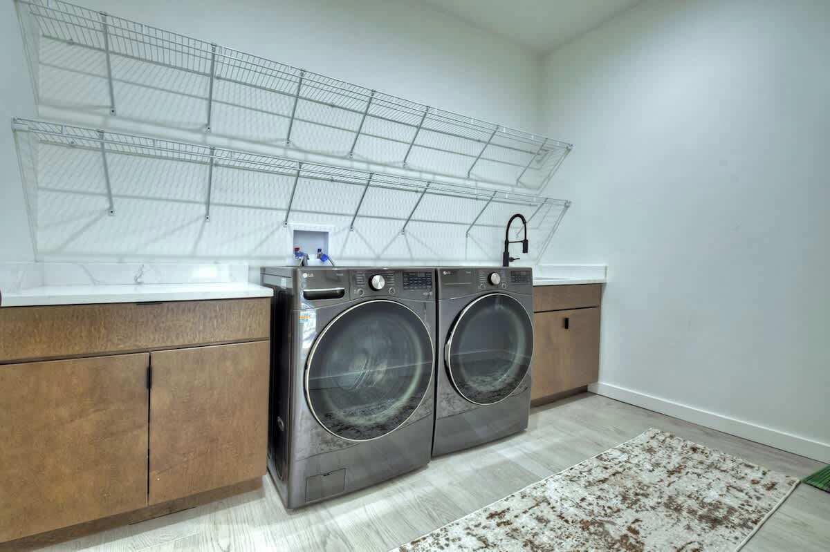 A laundry room with two front-loading washing machines, a metal drying rack, and a wooden cabinet.
