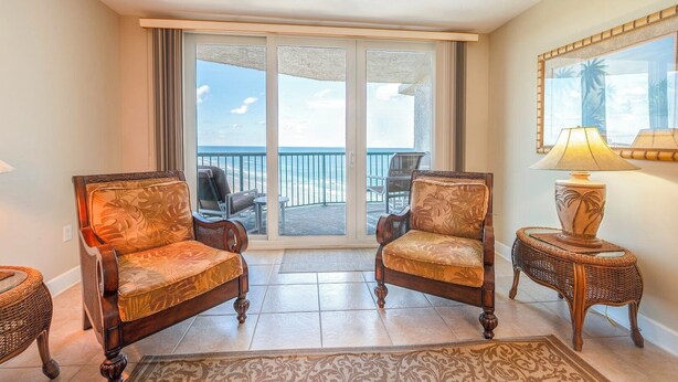 Una habitación con dos sillones tapizados, una mesita con lámpara y vista al océano a través de una puerta corrediza de vidrio.