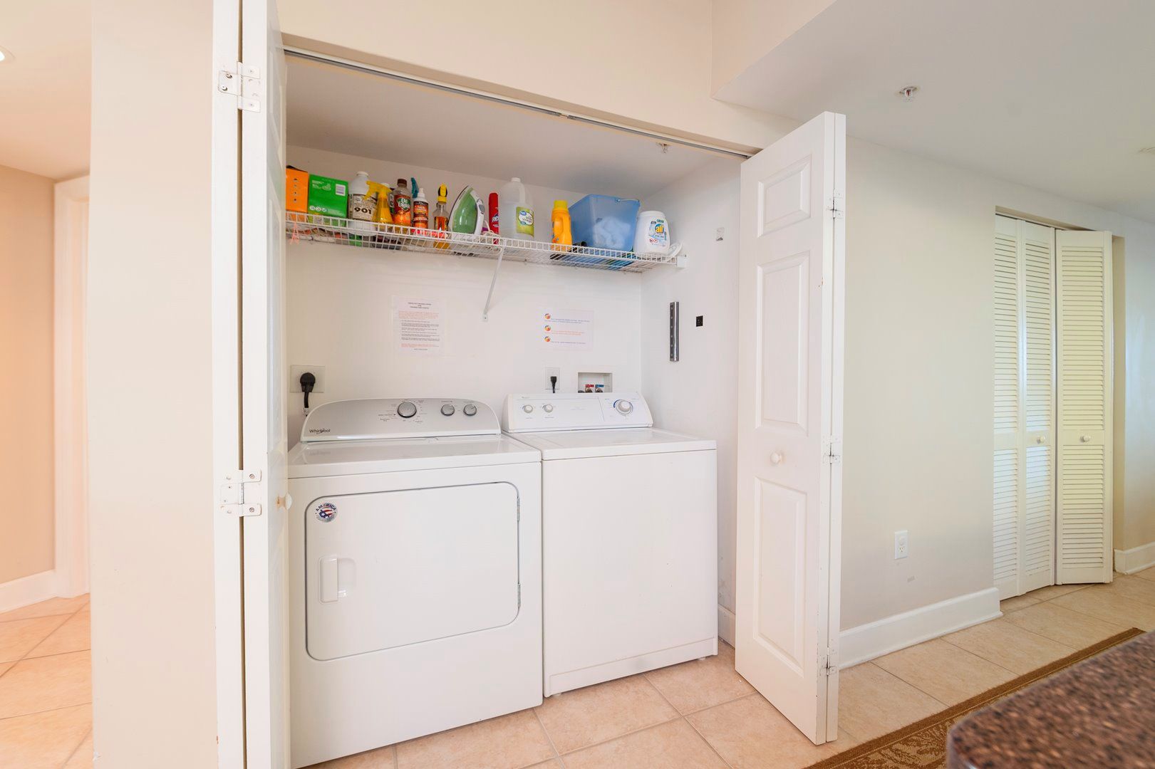 A laundry room with a washer and dryer, a shelf with cleaning supplies, and a door to a closet.