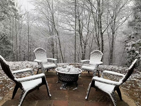 A patio area with four chairs and a table, surrounded by snow-covered trees.