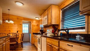A wooden interior with a kitchen, dining area, and a window with blinds. - Sleeps 6・Cozy Cabin・Spacious Outdoor・View・Firepit (Sevierville)