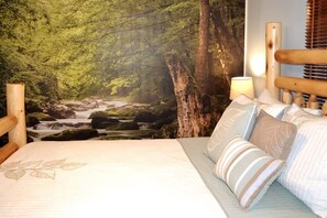 Quarto com cama, almofadas, cabeceira e um mural na parede com cena de floresta.