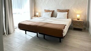 Ein modernes Hotelzimmer mit einem großen Bett, zwei Nachttischen mit Lampen, einem Fenster mit Vorhängen und einer strukturierten Wand.