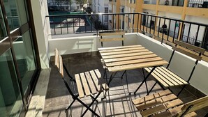 Ein Balkon mit Holztisch und -stühlen, Blick auf die Stadt und einem klaren Himmel.