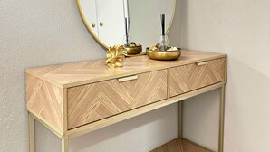 Ein Holzlager mit einem goldfarbenen Spiegelrahmen, einem goldenen Schmuckstück und einer kleinen Schale auf der Arbeitsplatte.