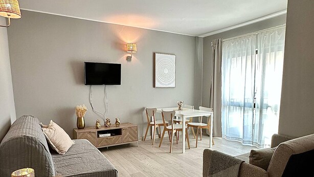 Ein modernes Wohnzimmer mit einer Couch, einem Couchtisch, einem an der Wand befestigten Fernseher und einem Essbereich mit Tisch und Stühlen.