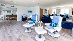 A spacious living area with a wooden floor, a blue sofa, two white armchairs, and a small round table. - Beach Front 5 Star Dog Friendly Home with Amazing Sea Views & Outdoor Kitchen (Portreath)