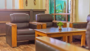 Un coin salon avec deux fauteuils en cuir marron et une table en bois, une petite plante en pot posée sur la table, et une fenêtre avec des rideaux.
