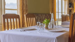 Une table à manger dressée avec des assiettes, des couverts et des verres, agrémentée d’un vase de fleurs et d’une bouteille posée sur la table.