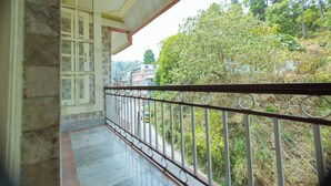 Un balcon doté d’une rambarde en métal, donnant sur un quartier résidentiel avec des arbres et des maisons.