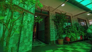 Une entrée d’immeuble avec un sol à carreaux, des plantes en pot et un plafond éclairé de lumière verte.