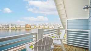 A balcony with white Adirondack chairs overlooking a waterfront with row houses.