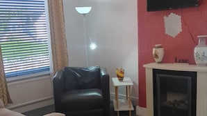 A living room with a black leather sofa, a small white table with a vase, a fireplace, and a window with blinds.