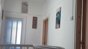 A hallway with white walls, a wooden door, and a window with vertical blinds.