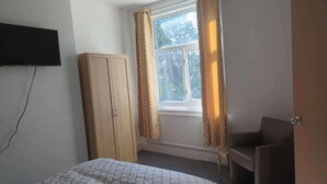 A bedroom with a bed, a wardrobe, a window with curtains, and a television mounted on the wall.