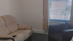 A living room with a beige sofa, a black armchair, and a patterned curtain.