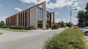 A modern building with a glass facade and vertical wooden panels, located beside a road with greenery and parked cars. - Bonington Student Village - Campus Accommodation (Sutton Bonington)