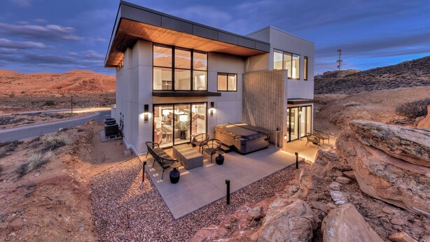 A modern two-story house with a spacious patio, large windows, and a view of the surrounding desert landscape. - Slickrock Luxury Retreat | Panoramic Views | Min to Trails and Ntl Parks (Moab)