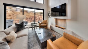 A modern living room with a large window, a fireplace, and a television mounted on the wall. - Slickrock Luxury Retreat | Panoramic Views | Min to Trails and Ntl Parks (Moab)