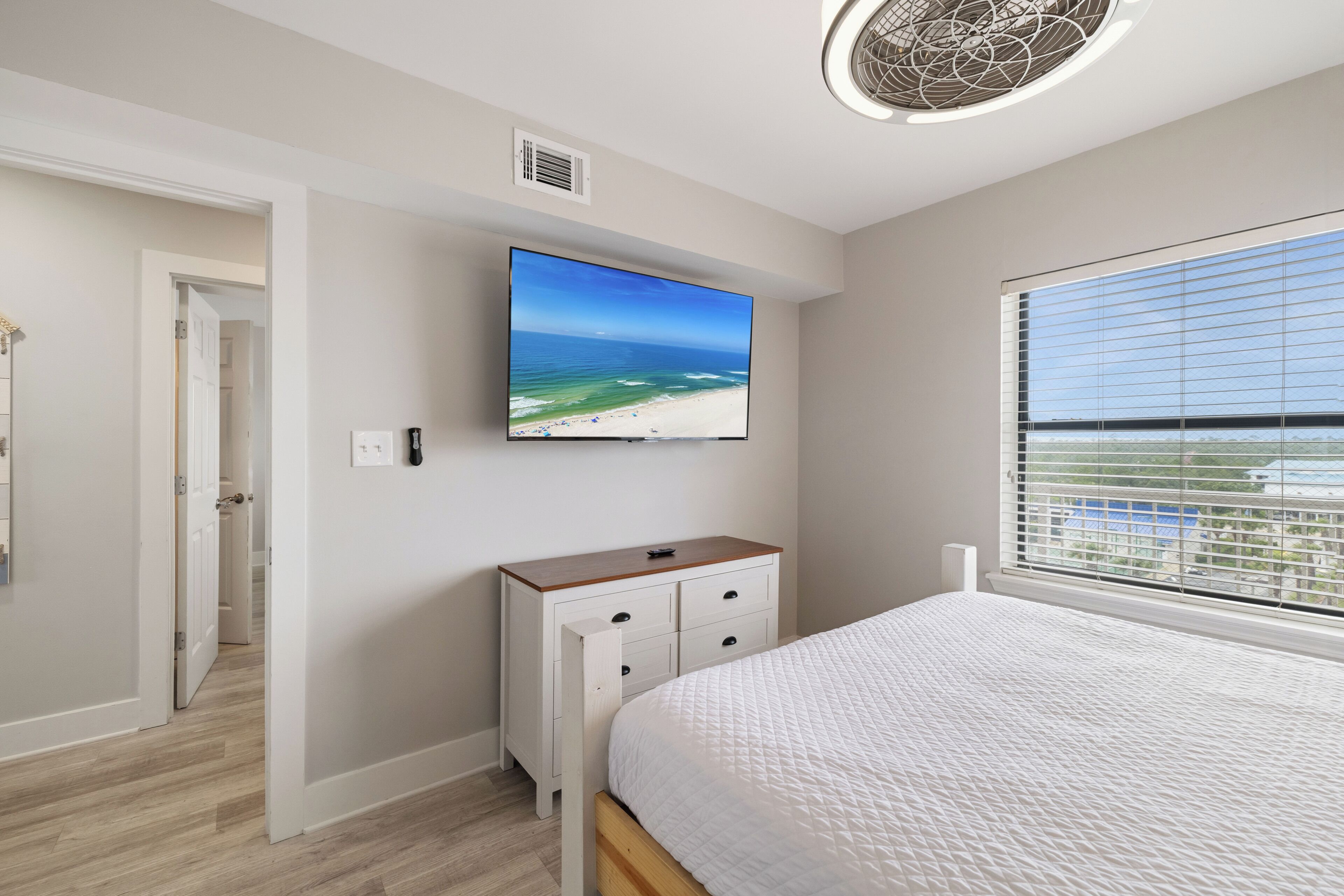 A bedroom with a bed, a TV on the wall, a dresser, and a window with blinds.